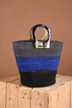 Black, blue, and gold woven bag on a wooden block with a brown background