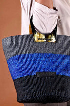 Tote bag with blue and black stripes held by a person against a brown background