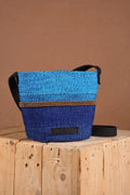 Blue woven bag with black accents on a wooden surface against a brown background. The bag is made from sustainably sourced sisal fibers