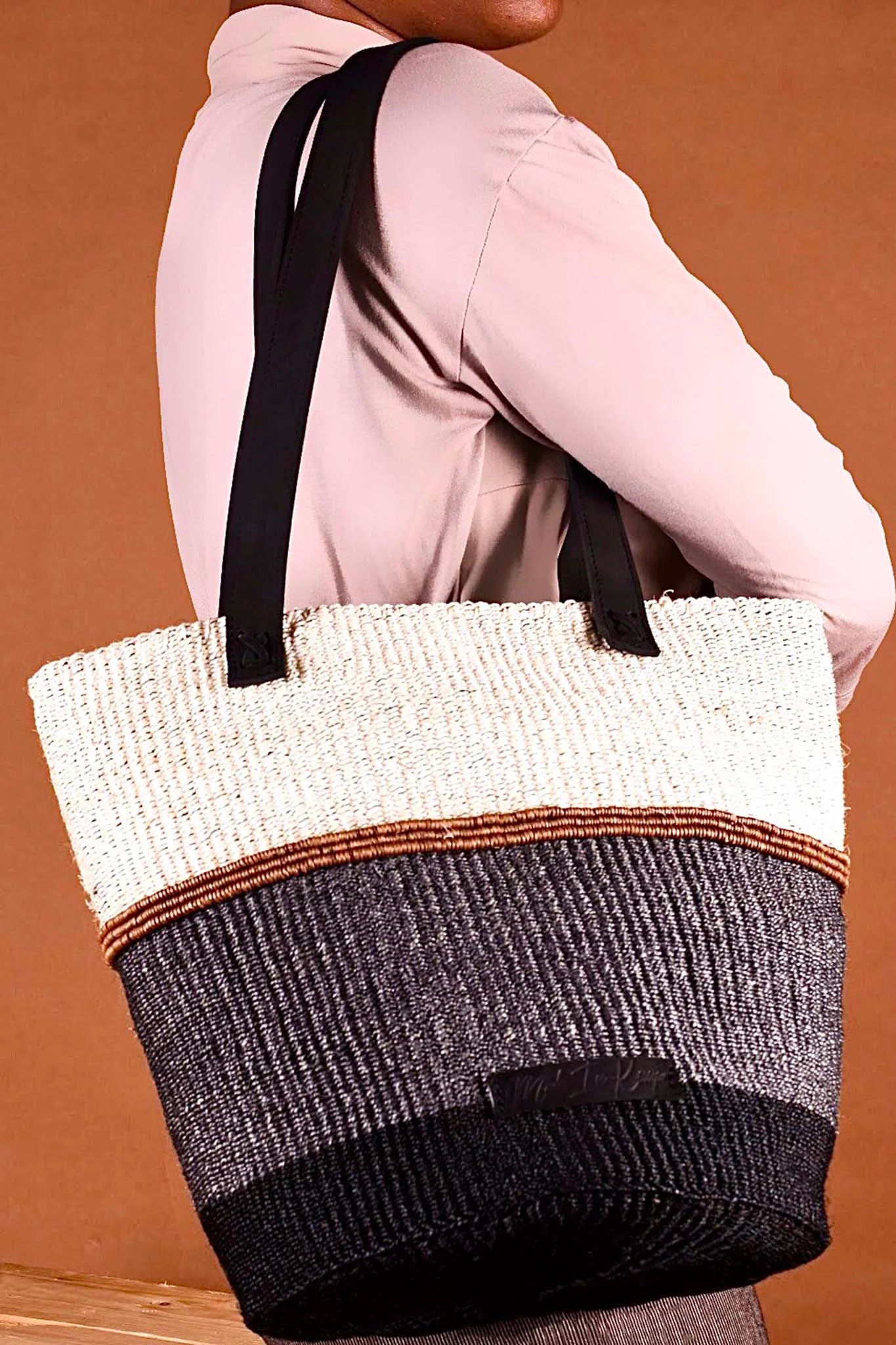 Person holding a woven tote bag with a gradient design against a brown background