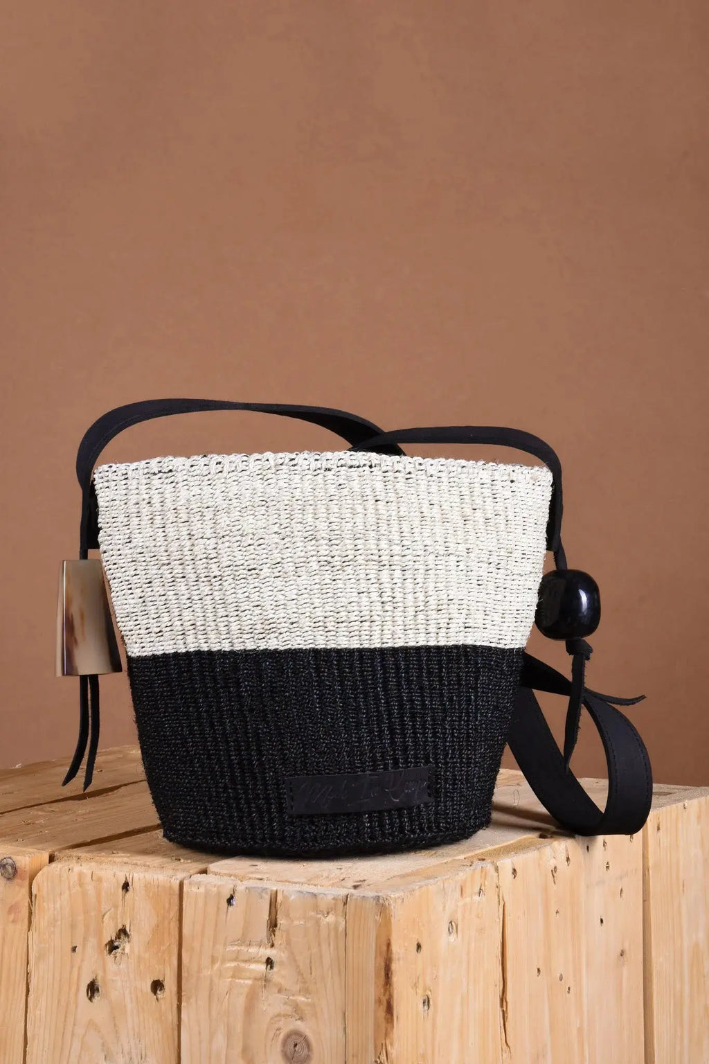 Woven handbag with black and white design on a wooden block against a brown background
