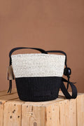Woven handbag with black and white design on a wooden block against a brown background