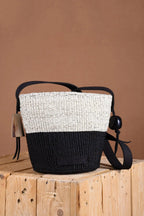 Woven handbag with black and white design on a wooden block against a brown background