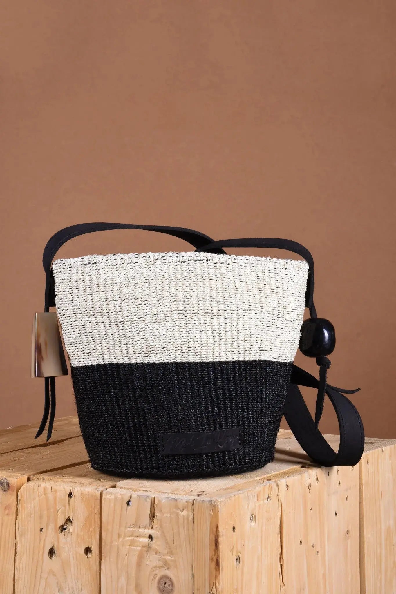 Woven handbag with black and white design on a wooden block against a brown background