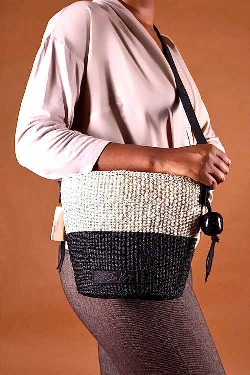Person holding a two-tone woven handbag with a plain background