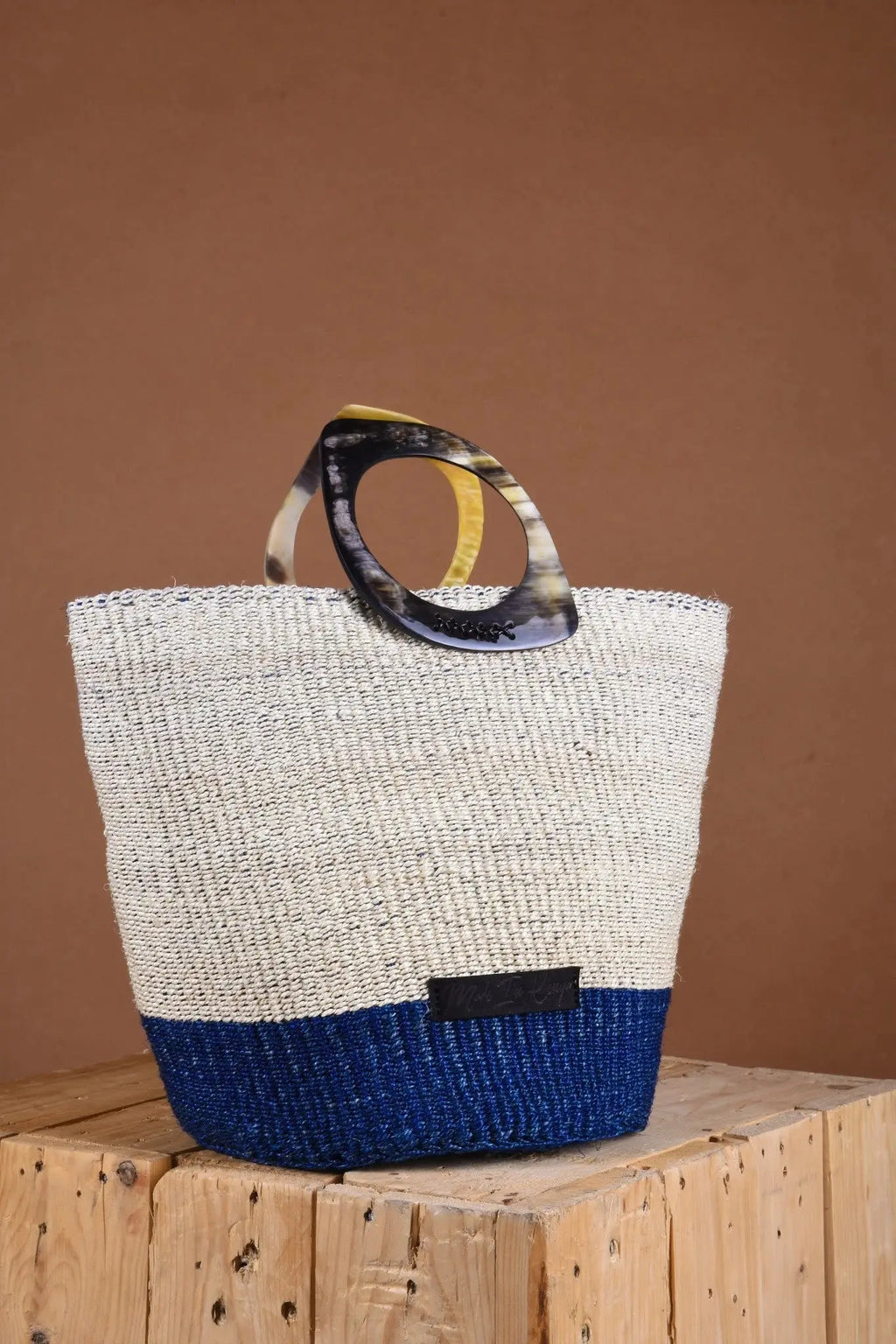 Woven bag with tortoiseshell handle on a wooden surface against a brown background