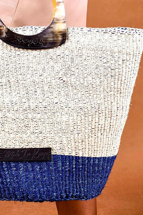 Woven handbag with white top and blue bottom on a brown background