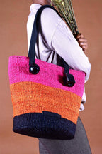Person holding a colorful striped bag with pink, orange, and navy sections against a brown background. 