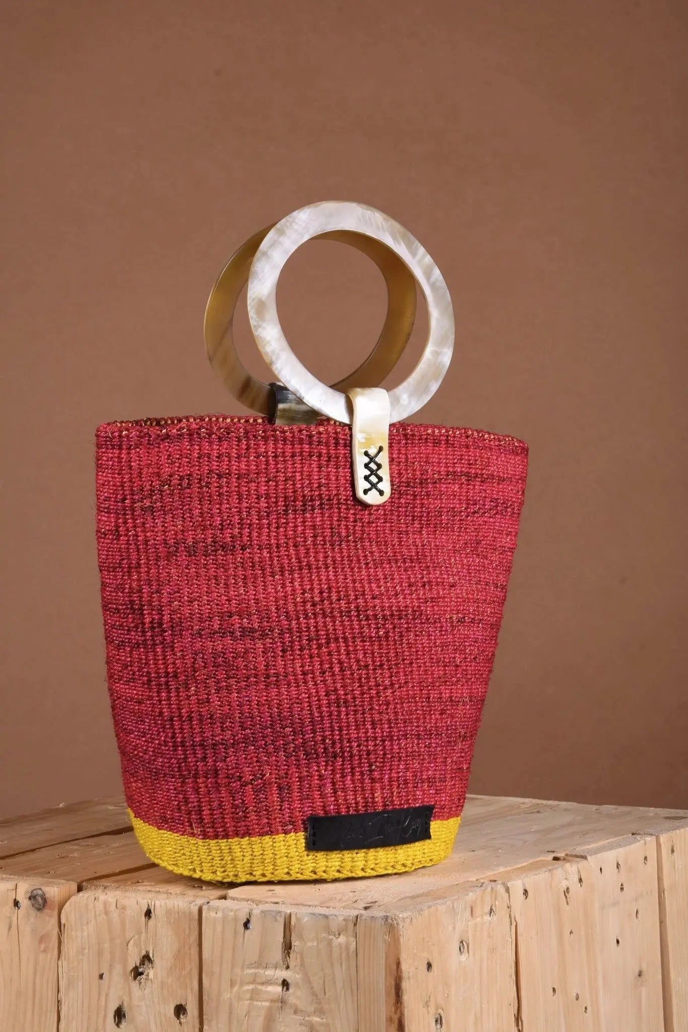 Red woven handbag with a yellow base and wooden handle on a wooden surface.