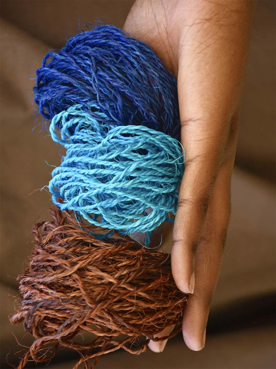 Three balls of yarn in brown, blue, and purple held in a hand against a blurred background.