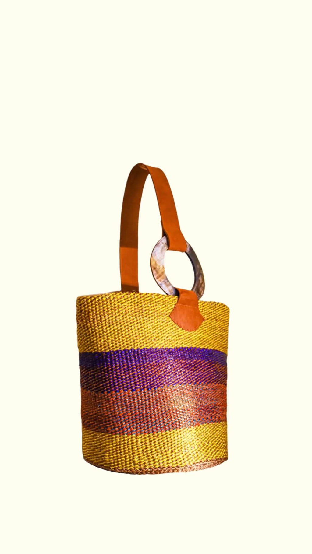 Colorful woven basket with a handle on a white background; the bag has leather handles, a yellow and vibrant look, and it was made by artisans from  Africa