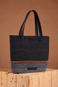 Black textured tote bag on a wooden block with a brown background