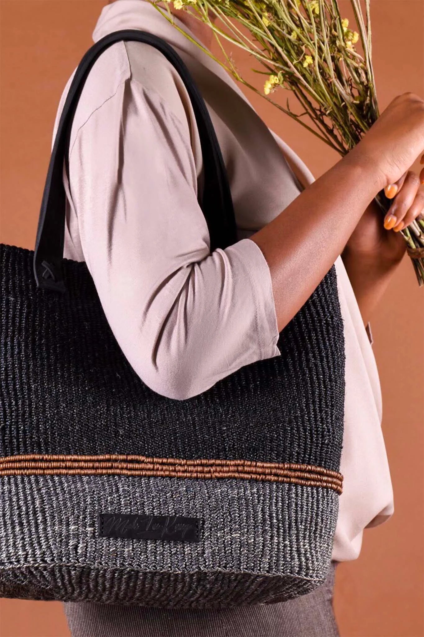 Person holding a textured black and gray tote bag with a brown accent against a warm-toned background.
