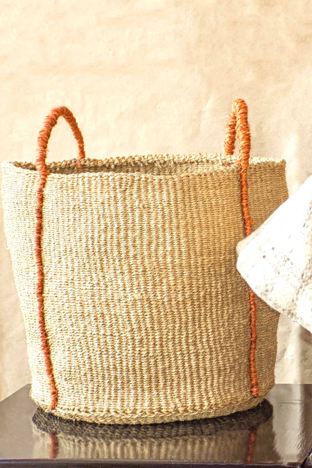 Woven basket with orange accents on a reflective surface