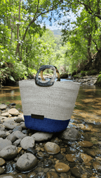 An artisan-made Tote bag with blue bottom section on a rocky stream with greenery